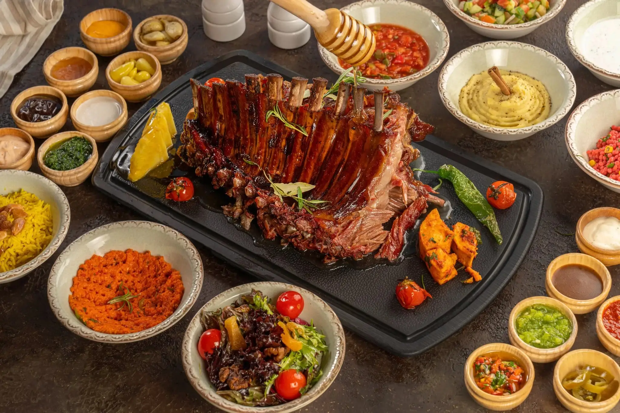 A rack of smoked halal lamb ribs with bowls of salads and dipping sauces